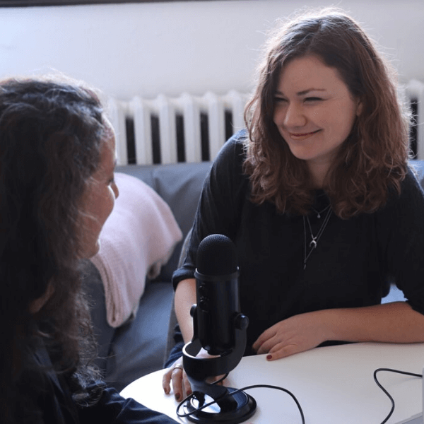 Two women sitting at a desk with a recording microphone in between them.