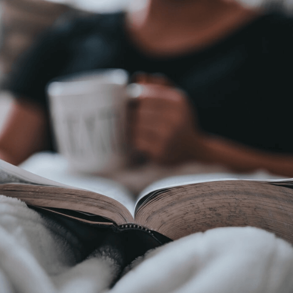 Person reading a book and holding a white coffee mug.