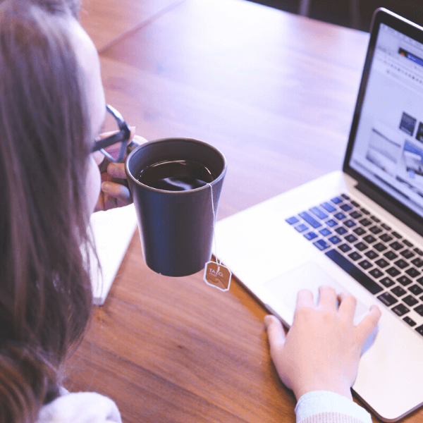 Woman looking at laptop and holding a cup of tea.