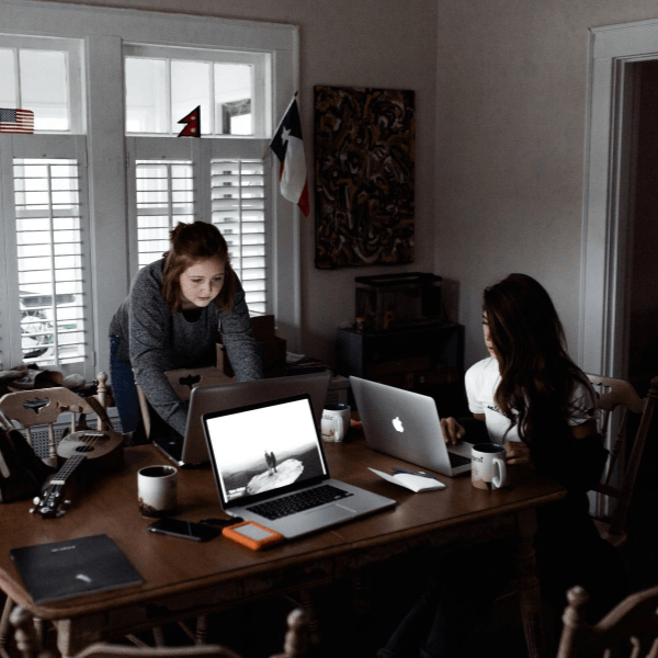 Two women working on lap tops and sitting at a table.