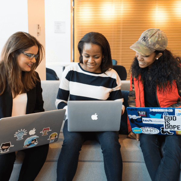 Three women are sitting on a couch while using laptops.