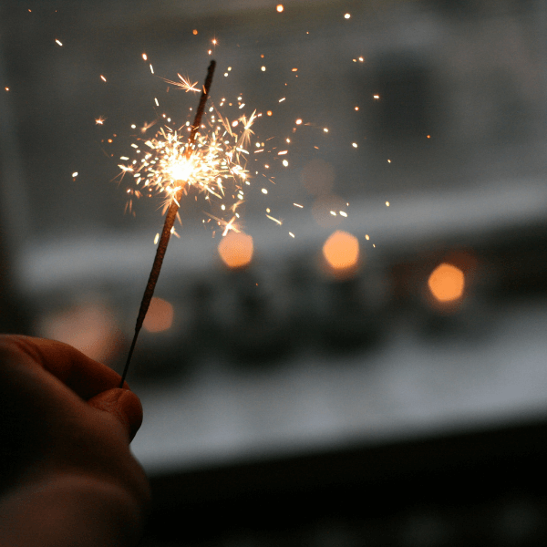 A hand holding a lit sparkler that has a sparkly flame.