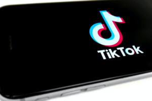 The logo of TikTok is displayed on an iPhone against a black screen.