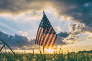 An American flag blowing in the wind in front of a sunset in a grass field