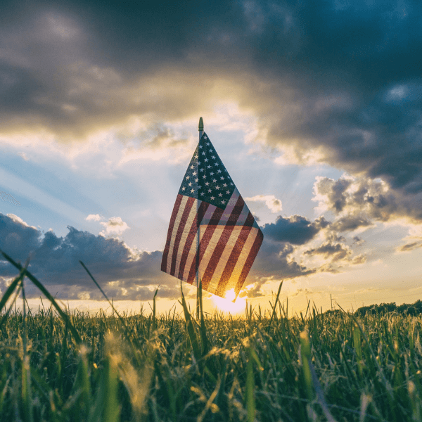 An American flag blowing in the wind in front of a sunset in a grass field