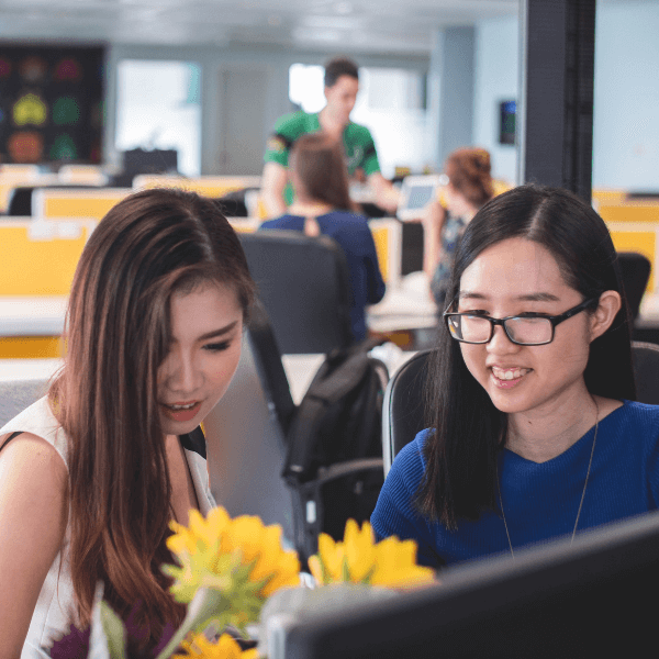 Two women sitting at a desk and smiling at a computer screen