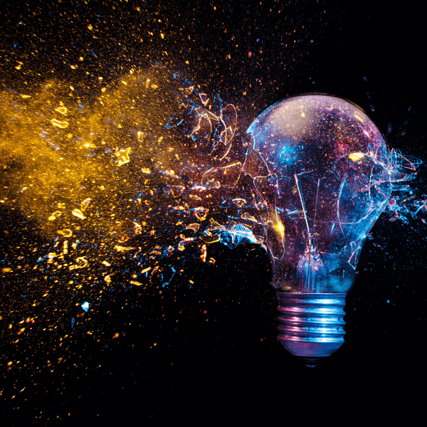 A photo of a lightbulb against a black background. Gold dust and multi-colored glitter is exploding from the light bulb.