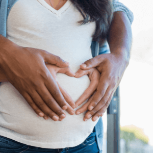 A close-up image of a pregnant woman's stomach, as she and her husband place their hands on where the baby is.