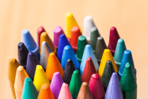 34 crayons of many different colors are tightly arranged in a clumped circle against a peach colored background