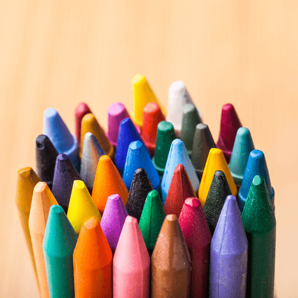 34 crayons of many different colors are tightly arranged in a clumped circle against a peach colored background