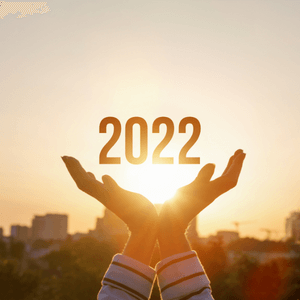 Two hands holding 2022, written out in gold, in front of a sunset. 