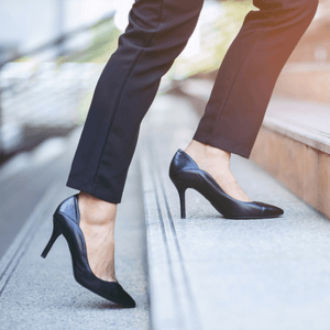 Photograph of a woman's high heels walking up a concrete staircase. 