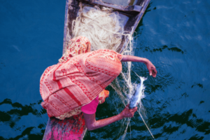 A woman sitting in a fishing boat in the ocean catching a fish.