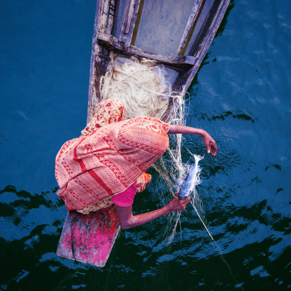 A woman sitting in a fishing boat in the ocean catching a fish.