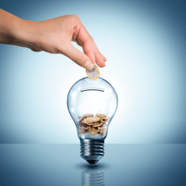 A hand places a coin into an unlit light bulb that is acting as a piggy bank. The image is against a light blue background.