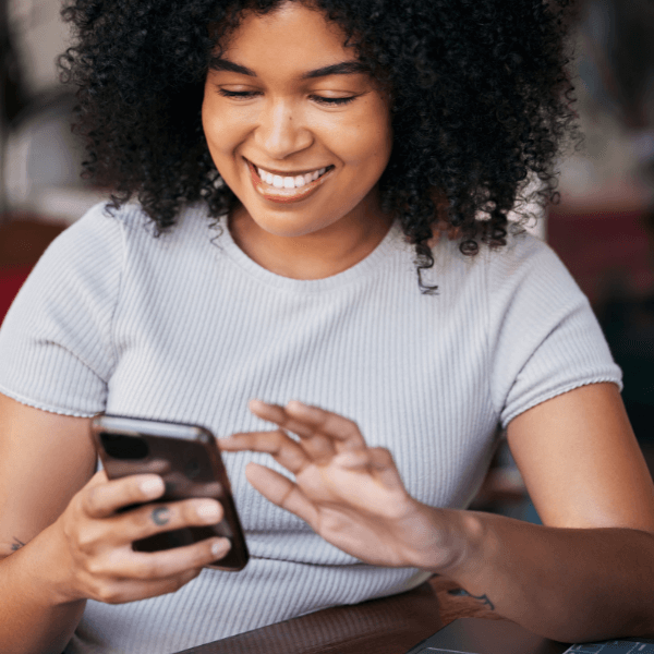 A woman is sitting in a chair as she is scrolling on her phone and reading what is on the screen.