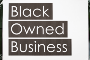A sheet of white paper is taped down on all four of its corners on a window. The paper reads "Black Owned Business."