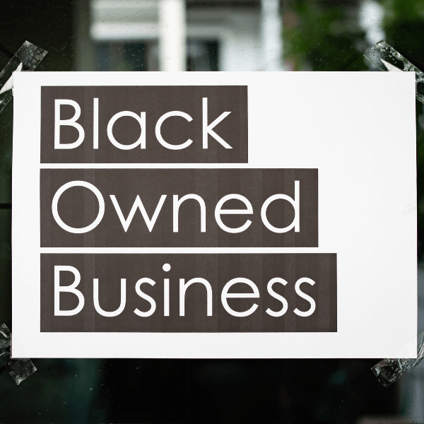 A sheet of white paper is taped down on all four of its corners on a window. The paper reads "Black Owned Business."