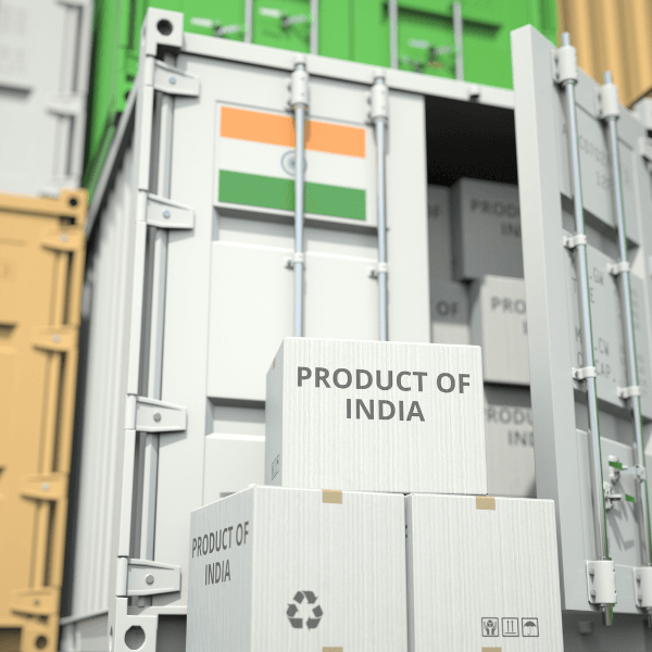 A white shipping crate is emblazoned with the flag of India, and two white shipping boxes sit in front of it, stacked one on top of the other, and the top box reads 'product of India.'