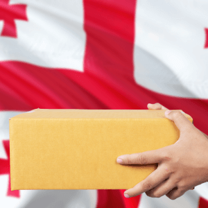 In front of the background of the flag of the country of Georgia, two hands hold a package.