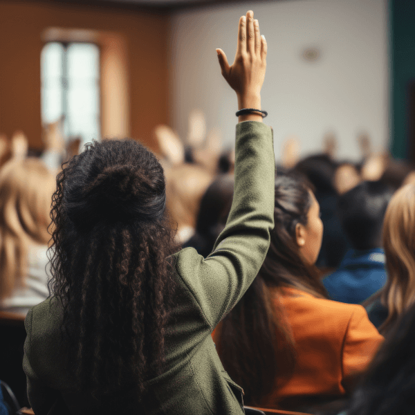 The back view of a woman raising her hand in a classroom full of other women.