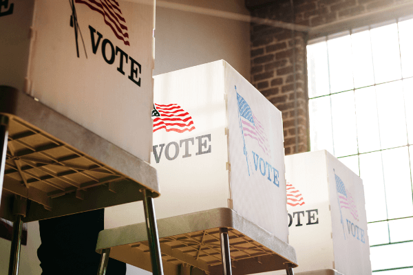 Three voting booths that have an American flag with the word "vote" depicted on the side.