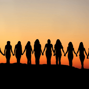 The silhouettes of 11 women holding hands in front of a sunset.