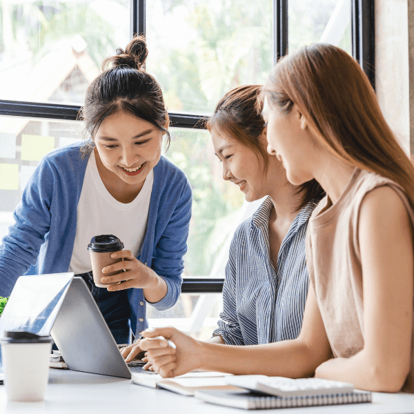 Three Vietnamese women sit at a laptop computer while having a conversation.