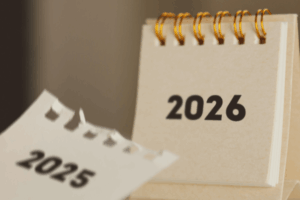A desk calendar notepad that has "2026" in black text with a torn paper falling to the desk that has "2025" in the same black font written on it.